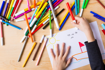 Kid's hand taking a red marking pen on a wood desk 