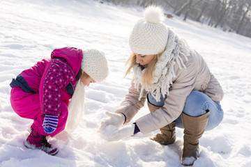 Mother having fun with daughter while making snowball