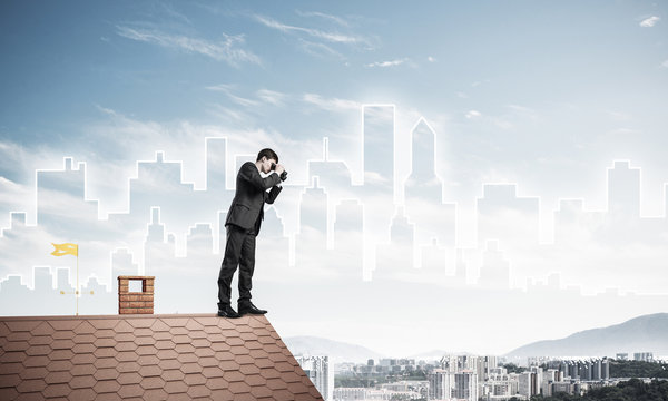Businessman standing on roof and looking in binoculars. Mixed me