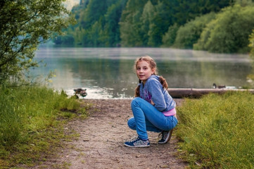 A girl child sits on the shore of a mountain lake.