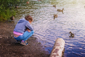 A girl child sits on the shore of a mountain lake.