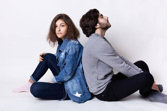 Thoughtful couple sitting on the floor back having rest. A young female dressed in jean clothes and stylish guy dressed casual clothes relaxing on the floor and dreaming about something