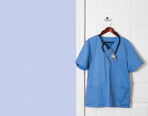 Blue scrubs shirt for medical professional hanging on door