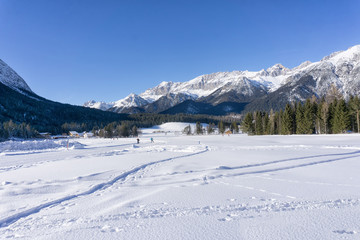 Winter mountains landscape with groomed ski track and blue sky in background