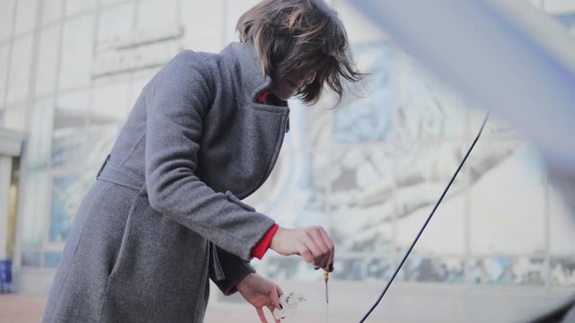Business woman checks the oil level in the car looking under the hood in the street. Putting back the dipstick