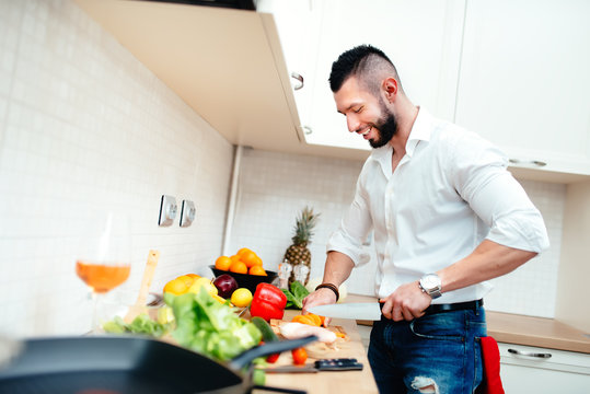 Happy smiling man cutting vegetables for salad or soup. Young professional well dressed cook preparing food in new kitchen