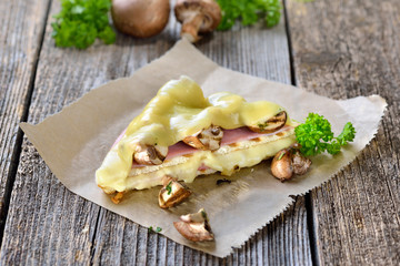 Heißes italienisches Panini mit Schinken, Käse und Champignons - Hot toast with ham, cheese and mushrooms served on sandwich paper on a wooden table