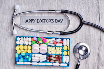 Drugs in organizer and stethoscope. Medical tools on wooden background. Happy doctor's day to you.