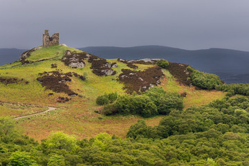 Fototapeta na wymiar North Coast, Scotland - June 6, 2012: On a bright green hilltop stand the remains of a castle tower near the village of Tongue under a dark gray sky. Foreground, hill with many hues of green.