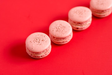 Strawberry macarons in a row, on a red background. These romantic french pastries are made of two meringue cookies and a sweet filling. Light & crisp, macaroons are the perfect valentine day dessert.