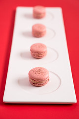 Strawberry macarons on a plate and red background. These romantic french pastries are made of meringue cookies and sweet filling. Light & crisp, these macaroons are the perfect valentine day dessert.
