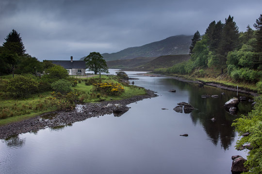 North Coast, Scotland - June 6, 2012: The shallow bluish gray reflecting Hope River meanders through a green landscape in front of tall mountains. Shades of green and yellow accents by broom flowers.