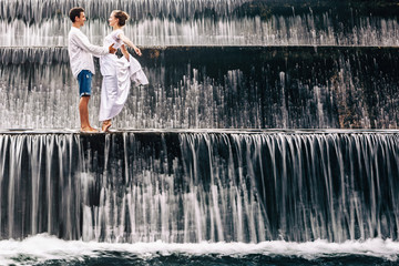 Fototapeta premium Happy family on honeymoon holidays - married loving couple hugging, kissing with fun under falling water in cascade waterfall pool. Active lifestyle, people travel on summer vacation on Bali island.