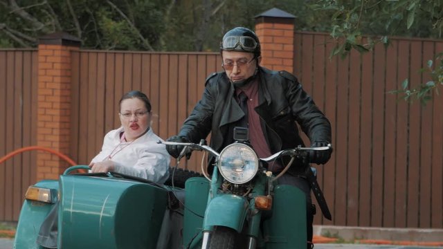 Biker ride in suburbs motorcycle with woman wears nurse costume grimacing in sidecar