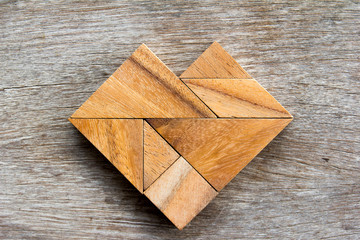 Tangram puzzle in heart shape on wooden background
