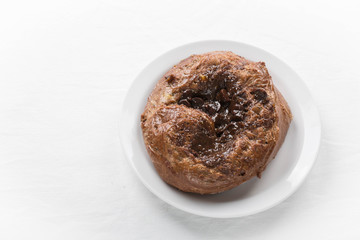 A chocolate custard bun on a white plate. Copy space. Horizontal photo. 
