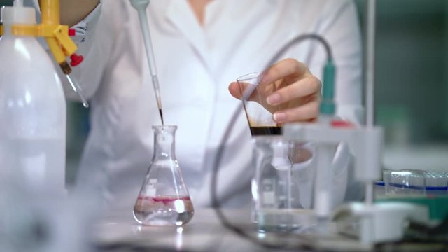 Chemical reaction in flask. Female scientist carrying out scientific research. Scientist woman dropping reagent in glass flask. Lab woman pouring liquid for chemical experiment in laboratory