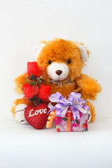 Brown teddy bear with a red rose and a gift box on a white background.