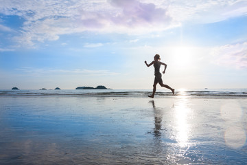 Silhouette of jogging woman at sunset or sunrise wet beach with beautiful reflection on sand. Healthy lifestyle, fitness concept.