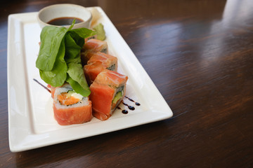 fusion salmon sushi rolls with sauce on white plate; healthy and fusion japanese food style concept