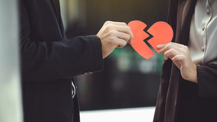 Man and woman pulling a red paper heart apart. The concept of un