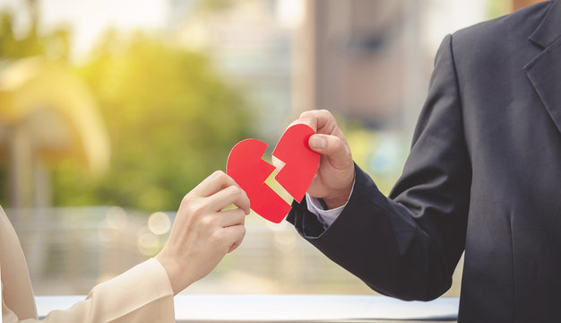 Man and woman pulling a red paper heart apart. The concept of un