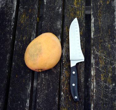 Mango and a big knife on an old weathered deck wooden board. Vertical wood background texture.