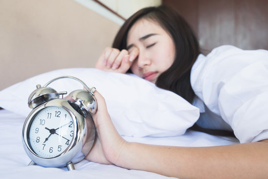  woman in bed trying to wake up with alarm clock.