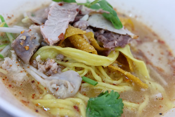 Bowl of Thai spicy noodles soup with pork and vegetables on table.