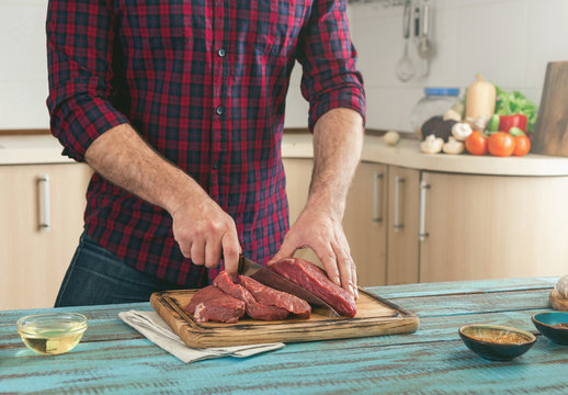 Man cuts piece of meat on wooden cutting board