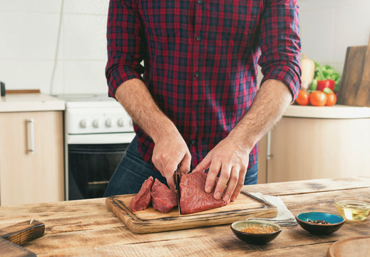 Man cooking beef meat on wooden table in the kitchen