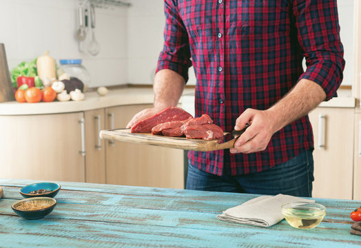 Man cooking meat on wooden table in the home kitchen