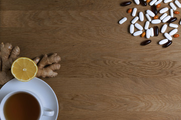 Choose between the traditional and folk medicine. Cup of tea, lemon, ginger, different pills on wooden background. Top view. Copy space. Health concept.