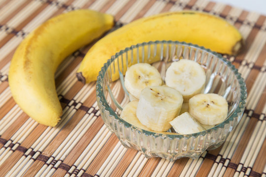 A banch of bananas and a sliced banana in a pot over a wood background.