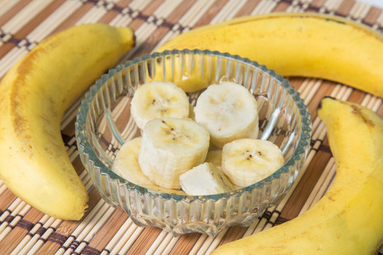 A banch of bananas and a sliced banana in a pot over a wood background.