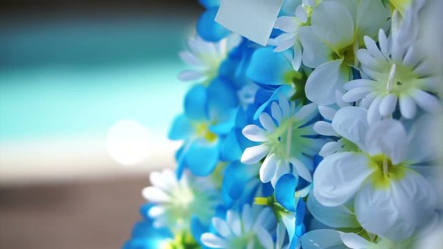 Blue and white artificial flower aloha hanging next to tropical pool