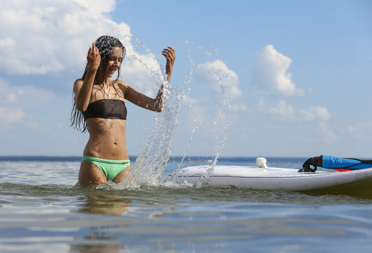 Young beautiful woman is sprinkling water of the sea near surf d