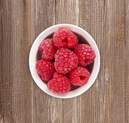 Raspberries in a white ceramic bowl. Ripe and tasty raspberries isolated on a wooden background. Top view.