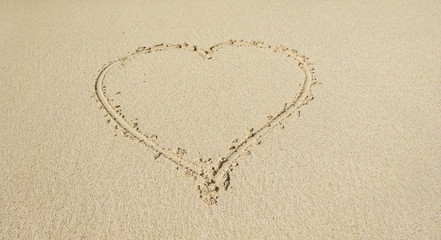Shape of a heart drawn on white sand tropical beach.