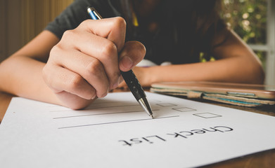 close- up hand holding pen on check list paper with tablet in vi