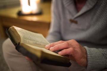 Unrecognizable man at home reading Bible, burning candles behind
