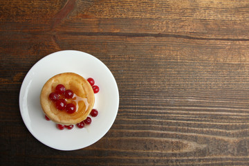 Pancakes with berries in the plate on a wooden background.