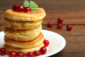 Pancakes with berries in the plate on a wooden background.