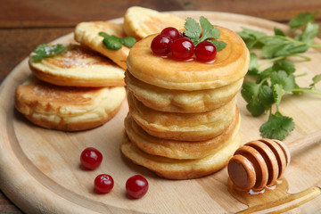 A stack of pancakes with berries and a spoon on a wooden tray.