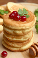 A stack of pancakes with berries and a spoon on a wooden tray.