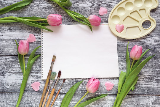 Art album, paintbrushes, palette and pink tulips on gray wooden