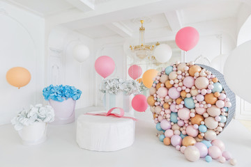 Boxes with flowers and a large pudrinitsa with balls and balloons in room decorated for birthday party.