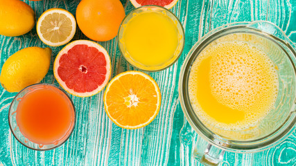 fresh juice from citrus fruits - lemon, grapefruit, orange, pine apple  in blender bowl and glasses on  turquoise colored wooden background, top view