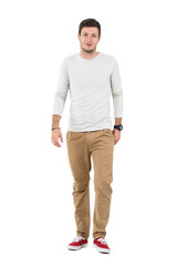 Fototapeta premium Friendly smiling man in beige pants walking towards camera. Full body length portrait isolated over white studio background. 