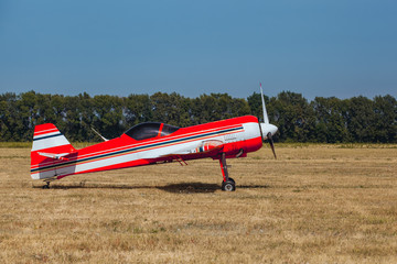 Small red and white private plane with propeller stands at the airport, in a bright, sunny day.